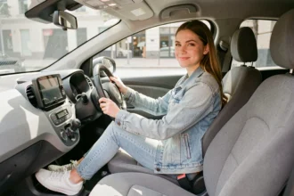 Jeune femme au volant d'une voiture sans permis compacte, souriante et confiante, intérieur moderne gris