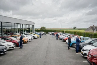 Vue panoramique d'un concessionnaire automobile en Vendée avec un large parvis de véhicules neufs et d'occasion, des clients et des vendeurs devant une façade vitrée moderne